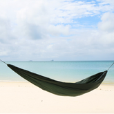 DD Superlight Hammock set up on a beach with calm water and clouds in the background, perfect for outdoor relaxation.